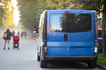 Fototapeta na wymiar Passenger van car parked on a city alley street side with blurred walking pedestrians in autumn.