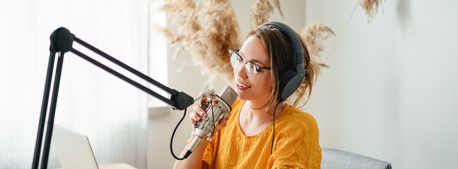 Cheerful woman podcaster recording her voice into microphone. Female radio host streaming podcast...