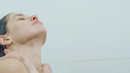 Close up woman standing under streams of cool water and enjoying process of taking shower in white shower in bathroom. Concept of young woman standing under streams of clean water.
