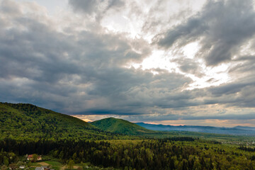 Fototapeta premium Aerial view of dark mountain hills covered with green mixed pine and lush forest in evening.