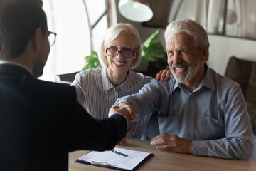 Excited mature couple shaking manager businessman realtor broker hand, greeting at meeting, happy satisfied senior family customers making successful insurance or investment deal, signing contract