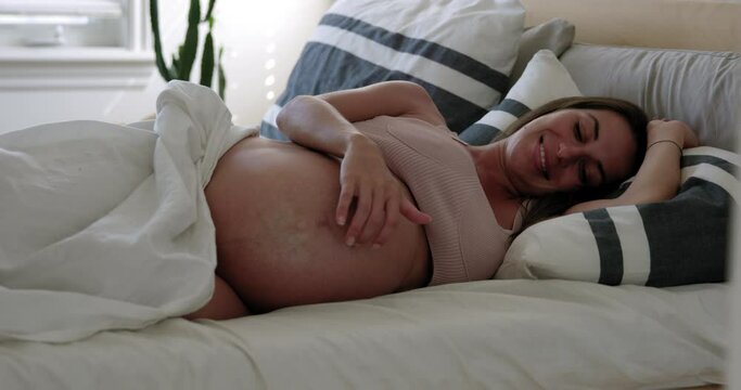 Pregnant woman wakes up and plays with belly smiling and happy