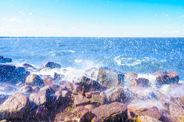 Splashing waves in the sunlight. Waves break on the coastal stones and turn into foam sea