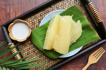 Boiled cassava or tapioca in syrup served with coconut milk - Thai dessert served in bamboo tray of the wood table