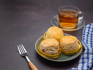 English style scones delicious freshly baked homemade on a plate with a cloth and a teacup on the old kitchen table. Space for text. Dessert and beverage concept.