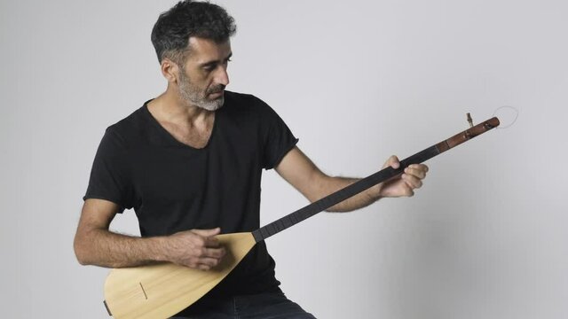 Middle eastern man playing Kopuz which is a string instrument named Baglama with three strings on a white background.