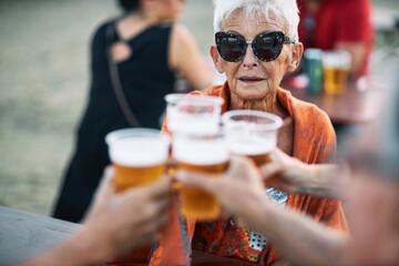 A very old woman with short gray hair is toasting with friends at a music festival. Fun has no age.