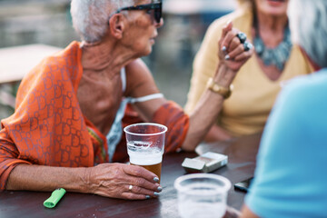 An old woman is sitting with her friends at a beer festival and drinking a new taste of beer. - obrazy, fototapety, plakaty