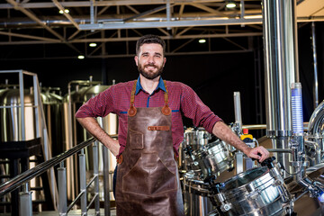 Fototapeta premium Young male brewer in leather apron supervising the process of beer fermentation at modern brewery factory