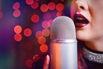 Female singer with disco mic on bokeh light background. Close-up of women's lips painted with burgundy lipstick and retro microphone. Redhead girl starting concert. Copy space for gig posters.