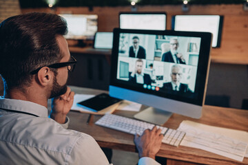 Fototapeta na wymiar Confident young man having video conference with the colleagues while staying late in the office