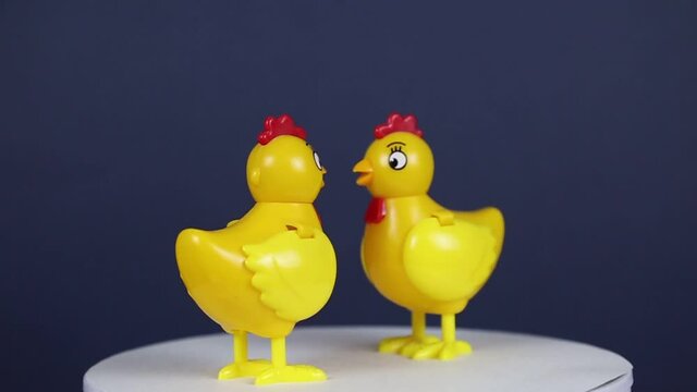 Figures of bright yellow chickens made of plastic are spinning on a dark background, the idea of a design concept with a copy of the space is to add text, traditions and objects.