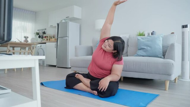Asian young oversize woman doing yoga exercise in living room at home.	