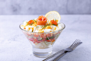 Layered salad with salted trout (salmon), caviar, eggs and vegetables. Traditional dish, one portion in a glass goblet on a gray background. Close-up.
