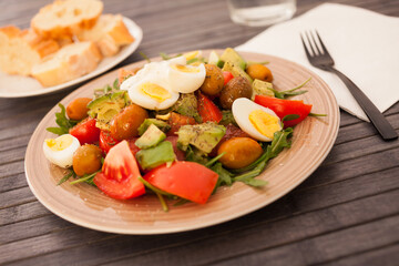 fresh salad of arugula, avocado, cherry tomatoes with olives and quail eggs on brown plate