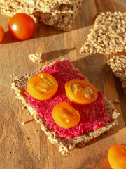 Seed crispbread with beetroot hummus and sliced cherry tomato on wooden background in the morning...
