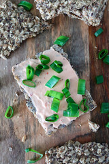 Seed crispbread with creme fraiche and green onion on wooden background