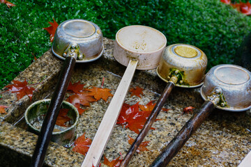 Ladles at a purification fountain with fallen red maple leaves in autumn fall season, in Kyoto, Japan