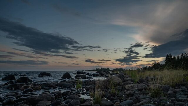 4K time lapse of Magnificent Soft and colorful sunset by the seaside stone. Beautiful cloud movement with seashore stones. Gradual light reduction.