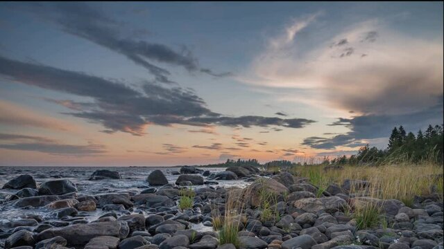 4K time lapse of Magnificent Soft and colorful sunset by the seaside stone. Beautiful cloud movement with seashore stones. Gradual light reduction.