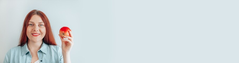 Portrait of a cheerful young woman eating red apple on gray wall background. Healthy nutrition diet. Apple vitamin snack.