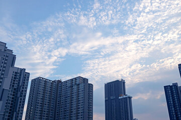 White Altocumulus Clouds Scattered on Light Blue Sky over the Group of Skyscrapers