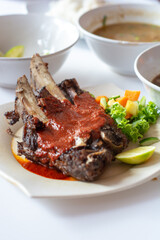 top view of grilled beef ribs with vegetables pickles and brown soup in plate