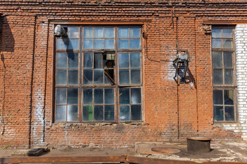 A large old dilapidated red and white brick house with large, dilapidated, crumbling windows. Old dirty abandoned factory building.