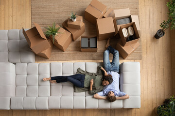 Top above view loving happy young family couple relaxing on huge comfortable couch near boxes with...