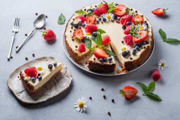 Cheesecake pie with fresh berries, strawberries, blueberries and blackberries and mint chamomiles in a round plate on a grey background.