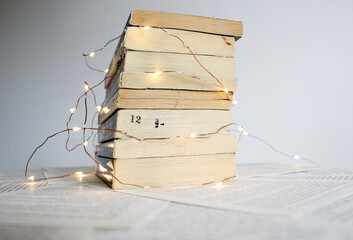 Stack of old paperback books with little Christmas or fairly lights strung around them.