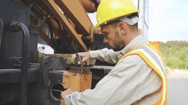 Mechanic with yellow hardhat repair heavy machine in construction site outdoors