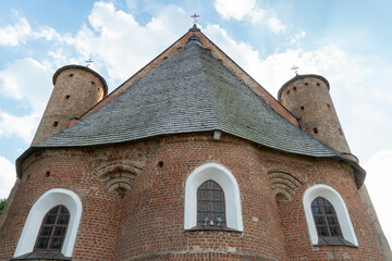 Fototapeta premium A beautiful old fortress church made of red brick against a blue sky background. Beautiful tiled roof of a medieval castle and white arched windows.