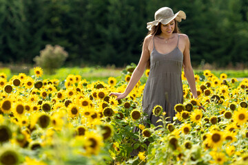 beautiful woman walking in a field of sunflowers in a linean country style dress and straw hat