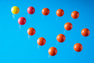 Arrow of red spheres and a yellow one on top of it on blue background.