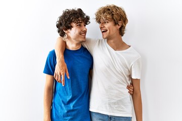 Fototapeta premium Young gay couple standing together over isolated background looking away to side with smile on face, natural expression. laughing confident.
