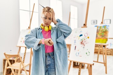 Young caucasian girl at art studio looking at the watch time worried, afraid of getting late