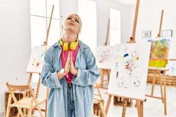 Young caucasian girl at art studio begging and praying with hands together with hope expression on...