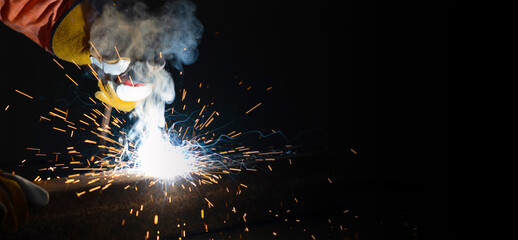 Closeup metal industry worker's hand welding steel sheet. Sparkler on black background. Heavy work in factory.