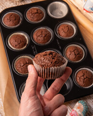 man holding a chocolate muffin on wood background. chocolate muffin in hand close-up over the kitchen table. Homemade cupcakes in the morning.