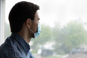 Thoughtful depressed millennial man looking out of window with hope, thinking over business lockdown loss, future vision after epidemic quarantine, coronavirus pandemic, feeling doubt, uncertain