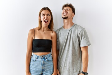 Naklejka premium Young beautiful couple standing together over isolated background angry and mad screaming frustrated and furious, shouting with anger. rage and aggressive concept.
