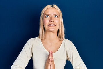 Beautiful blonde woman wearing casual sweater begging and praying with hands together with hope...