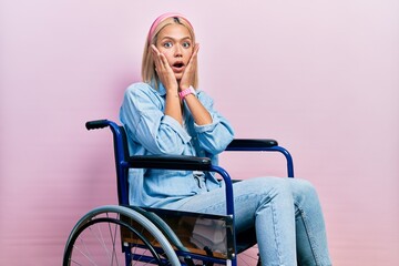Beautiful blonde woman sitting on wheelchair afraid and shocked, surprise and amazed expression...