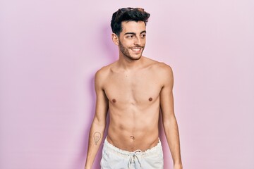 Fototapeta premium Young hispanic man wearing swimwear shirtless looking away to side with smile on face, natural expression. laughing confident.
