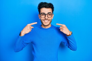 Young hispanic man wearing casual clothes and glasses smiling cheerful showing and pointing with fingers teeth and mouth. dental health concept.