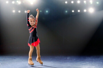 Little skater rides on rings in red and black dress on ice arena
