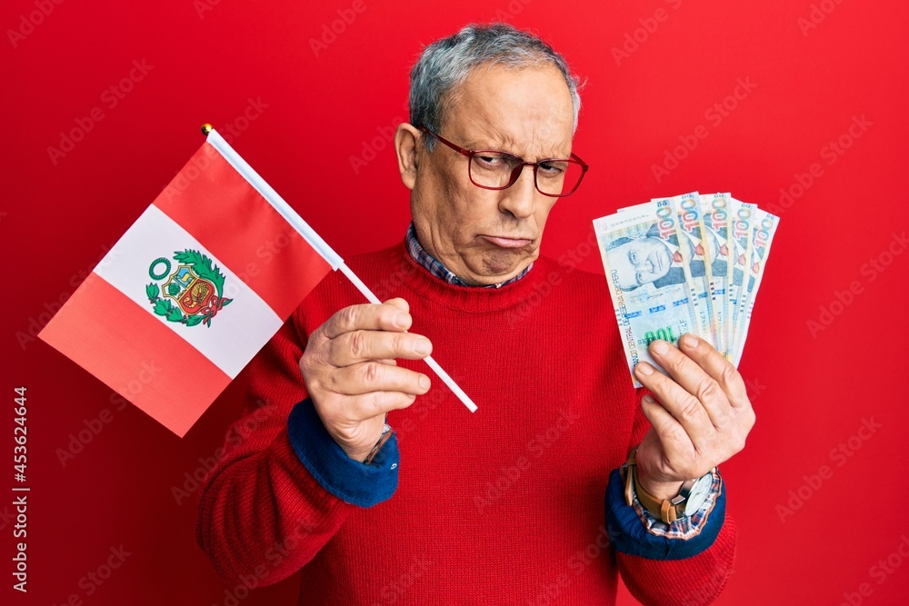 Poster handsome senior man with grey hair holding peru flag and peruvian sol banknotes depressed and worry 