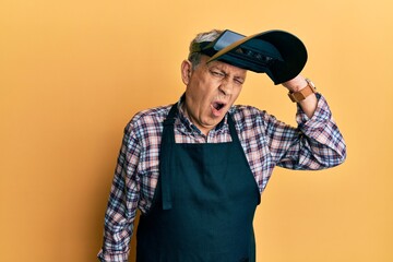 Handsome senior man with grey hair wearing welding protection mask confuse and wonder about question. uncertain with doubt, thinking with hand on head. pensive concept.