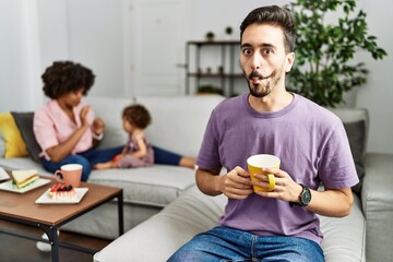 Hispanic father of interracial family drinking a cup coffee making fish face with lips, crazy and comical gesture. funny expression.